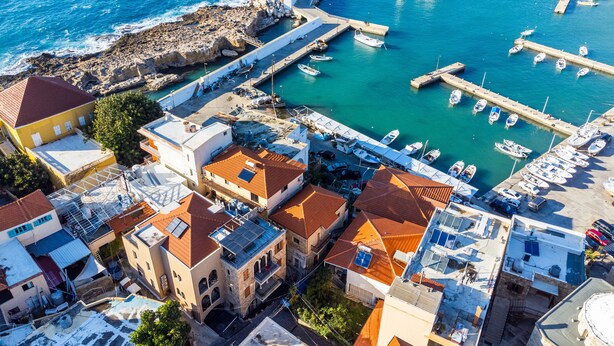 An aerial view of a coastal town with a marina, buildings with red-tiled roofs, and a lighthouse. - Bubble Beach 2-BR in Souk Batroun with Parking
 (Batroun)