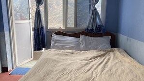 Une chambre à coucher avec un lit, une fenêtre avec des rideaux et une vue sur un paysage montagneux.