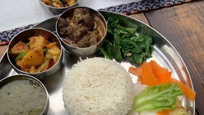 Un plat traditionnel servi dans une assiette en acier inoxydable, accompagné de riz, de légumes et de différents types de curry.
