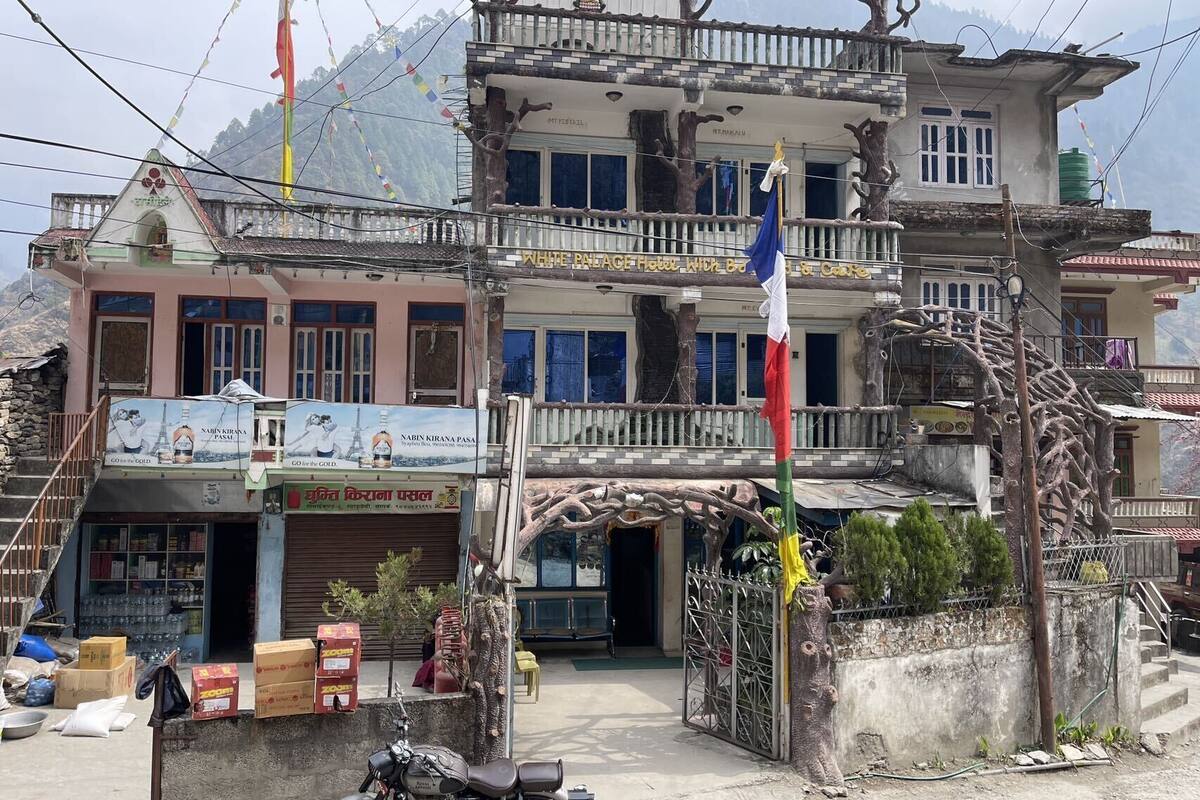 A multi-story building with a balcony, a sign for a hotel, and a motorcycle parked in front.