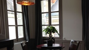 A dining area with a table and chairs, a hanging light fixture, and a view of the outside through large windows.