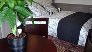 A neatly arranged bedroom with a bed, bedside lamps, a potted plant, and a small table.