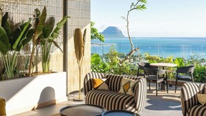 A modern outdoor living space with a view of the ocean, featuring a sofa, chairs, and a table. - Legend Hill Residences & Spa (Black River)