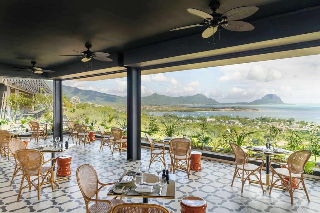 Un espace extérieur aménagé pour les repas, avec des chaises et des tables en osier, offrant une vue panoramique sur les montagnes et la mer.