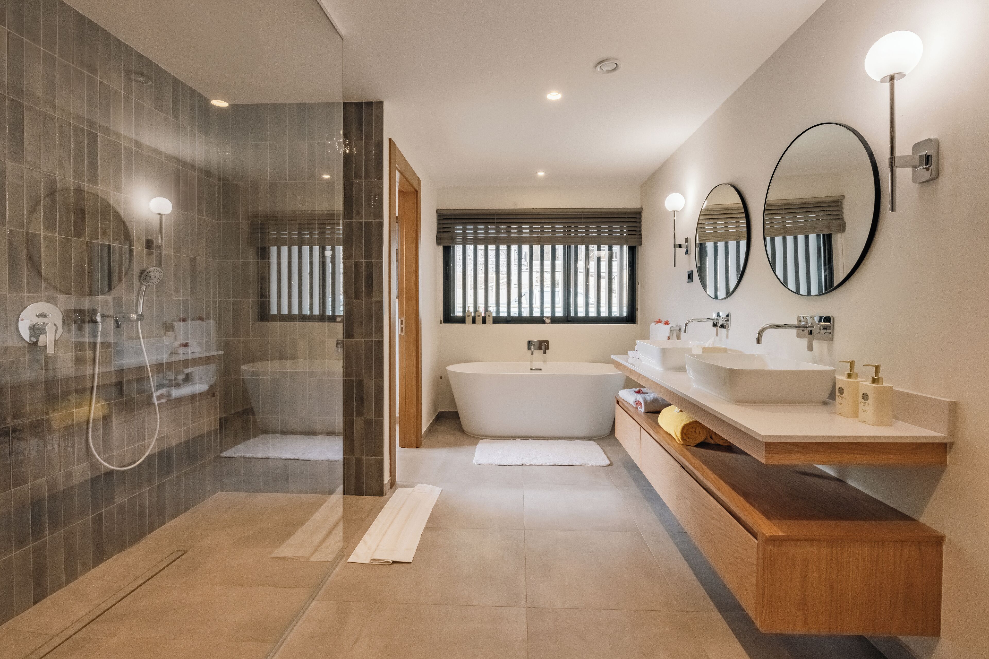 Un baño moderno con ducha a ras de suelo, bañera independiente y tocador con espejo.