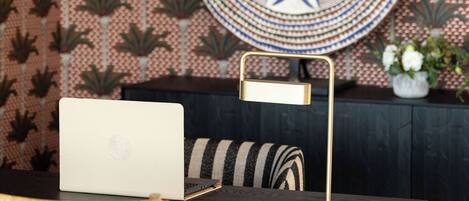 A room with a patterned wallpaper, a round decorative plate, a laptop on a table, a chair, and a small potted plant.
