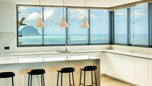 A modern kitchen with a large window overlooking the ocean, a white countertop, and three black bar stools. - Legend Hill Residences & Spa (Black River)