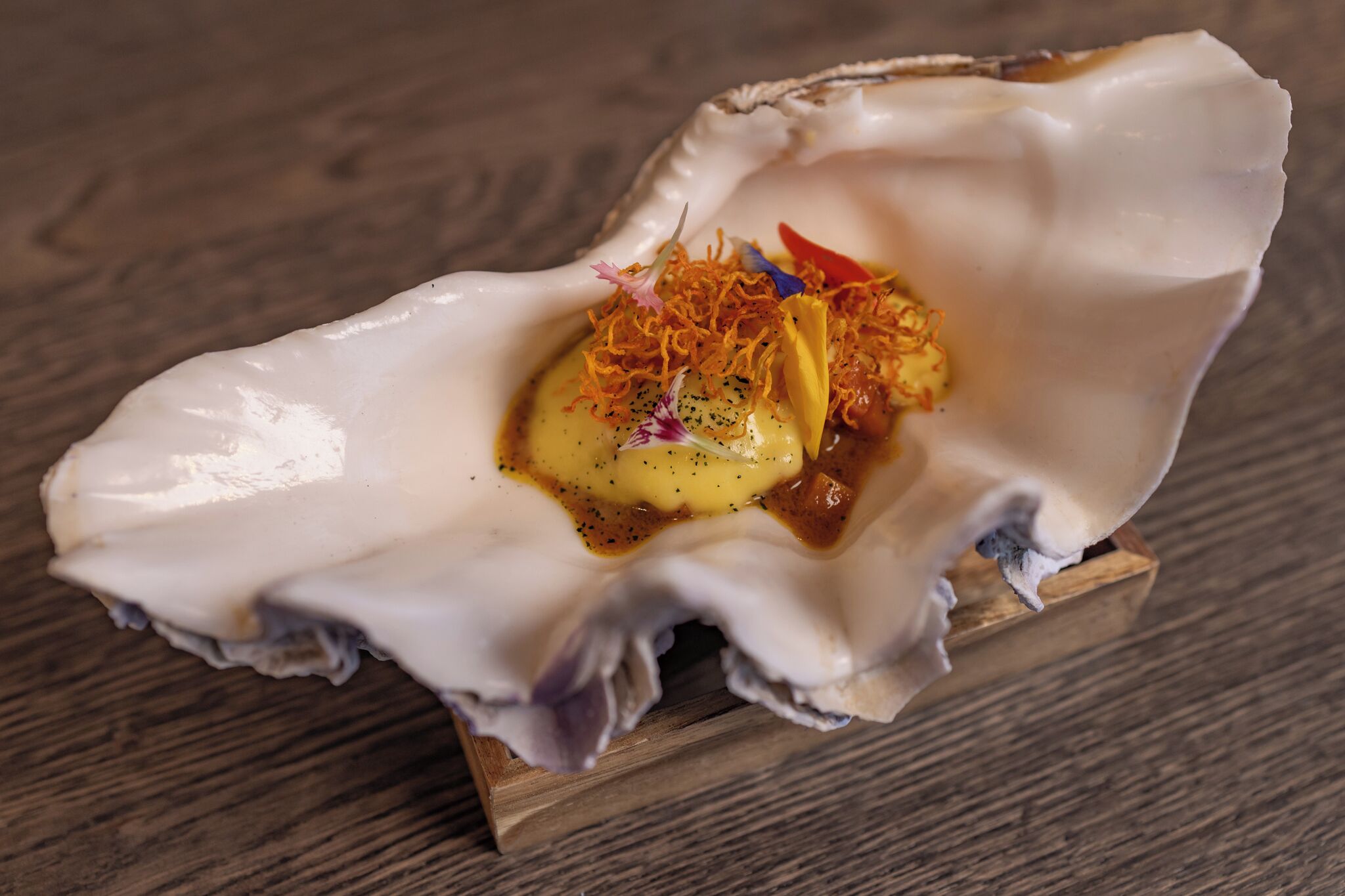 A dish served in an oyster shell with a wooden base.