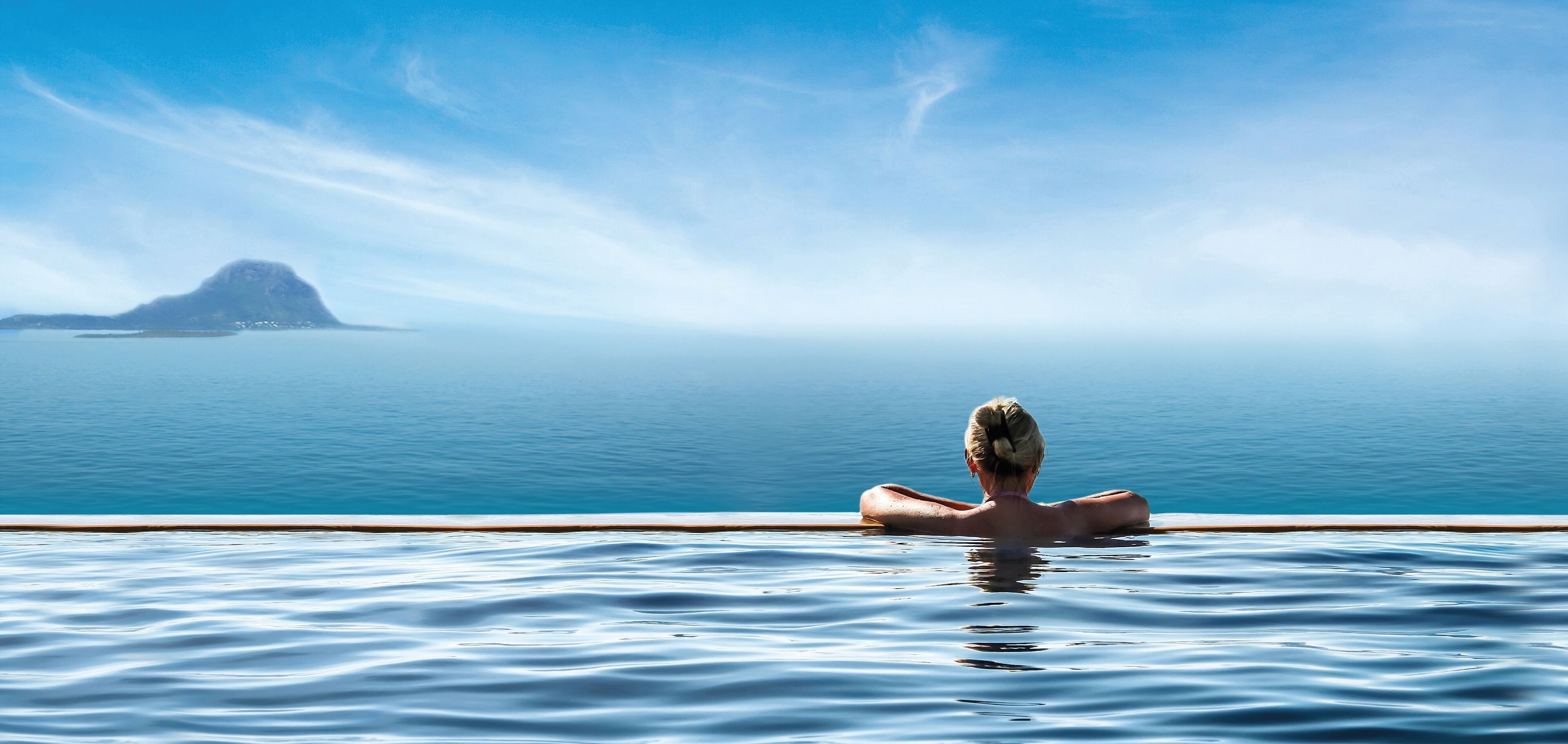 Una persona descansando en una piscina con vista al mar y una isla distante.