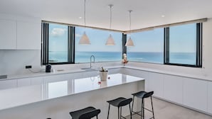 A modern kitchen with a large island, bar stools, and a view of the ocean. - Legend Hill Residences & Spa (Black River)