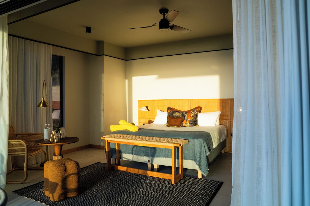 A hotel room with a bed, a small table, a chair, and a ceiling fan.