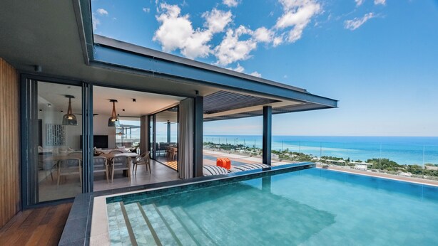 A modern poolside area with a clear view of the ocean, a covered seating area, and a glass-enclosed space with furniture. - Legend Hill Residences & Spa (Black River)