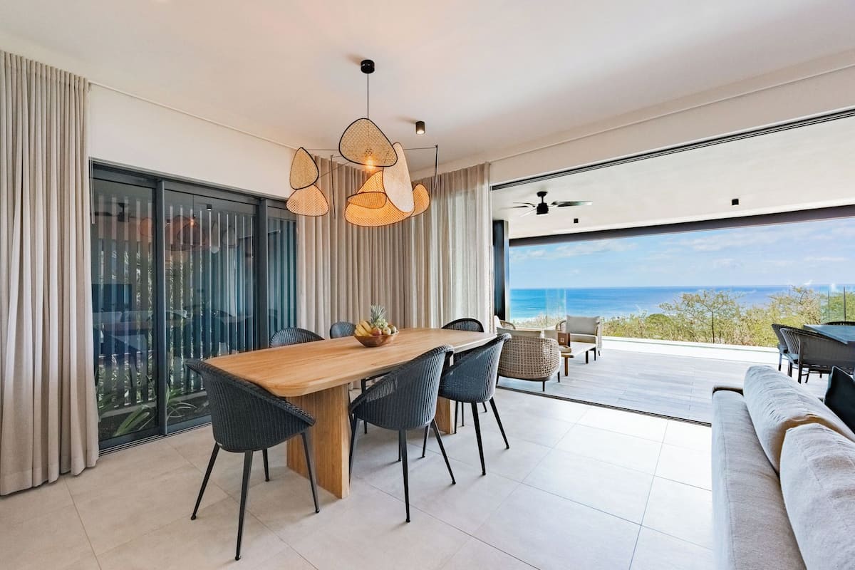 A modern dining area with a wooden table, black chairs, and a view of the ocean.
