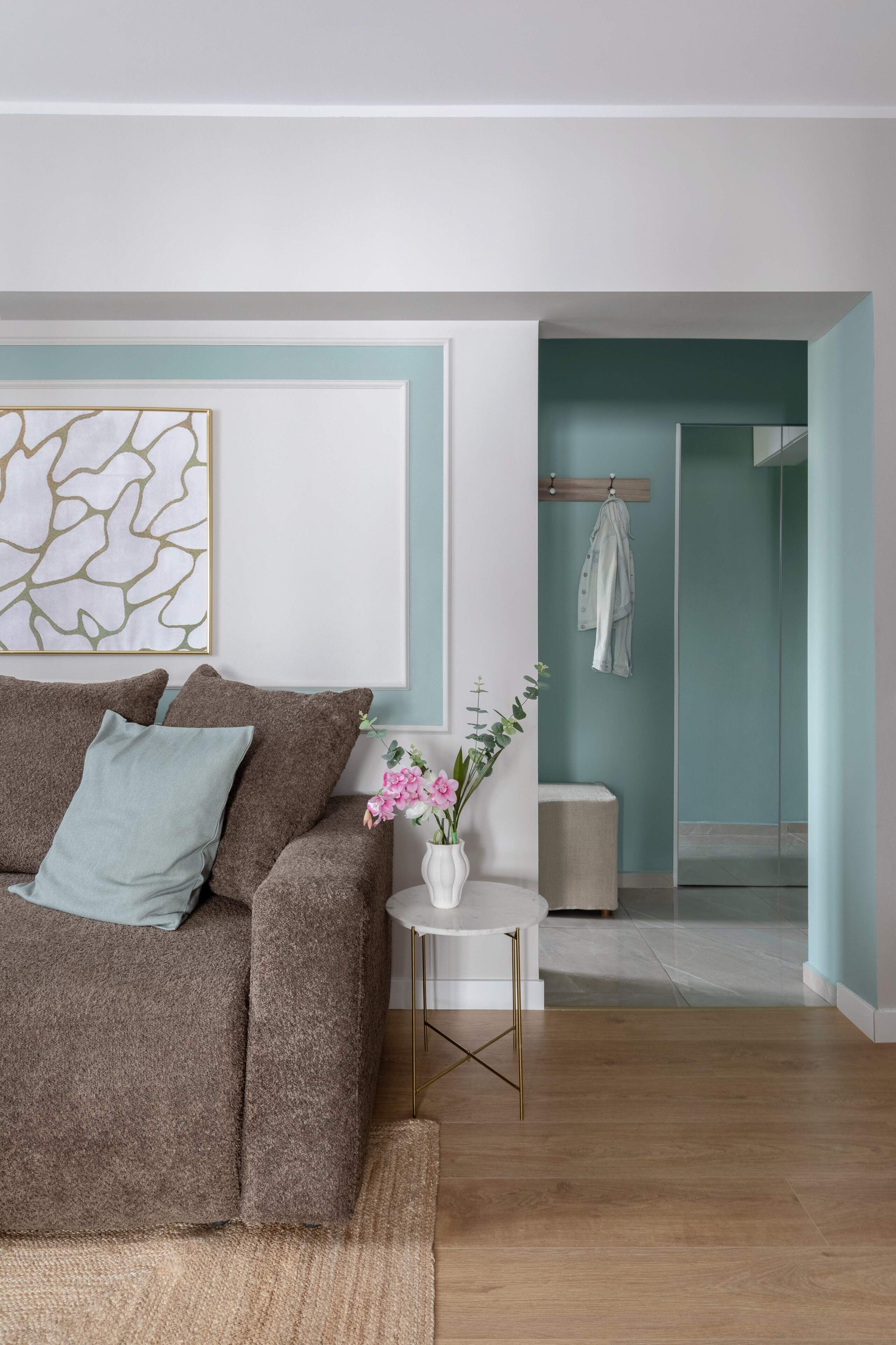 A modern living room with a brown sofa, a small white side table, and a vase with flowers.