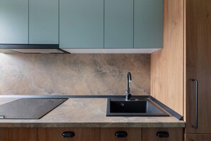 A modern kitchen with a marble countertop, black sink, and wooden cabinets. - Sublime Minty Green 1BR on the Park (Bucharest)