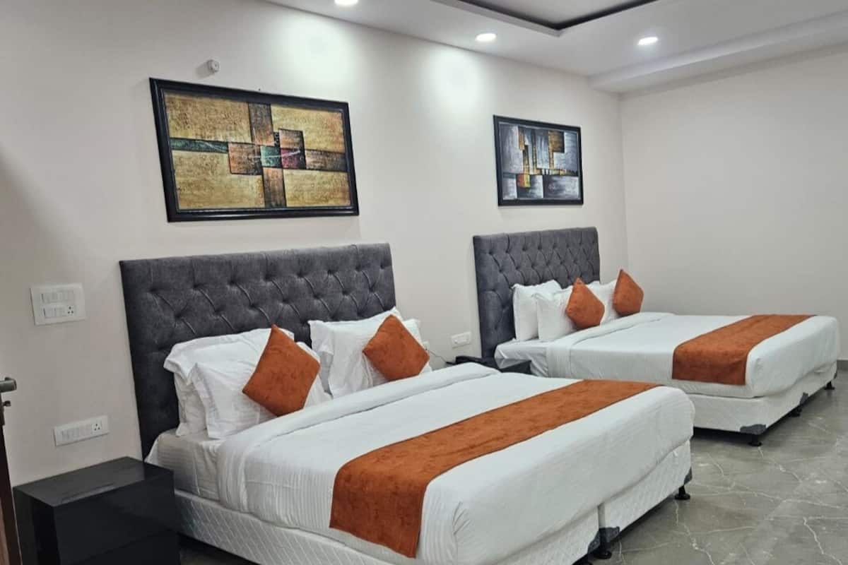 Ein Hotelzimmer mit zwei Betten, jeweils mit grauem Kopfteil und weißer Bettwäsche. Darüber an der Wand befinden sich zwei gerahmte Kunstwerke.