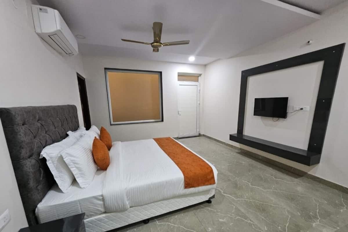 Ein Hotelzimmer mit Bett, Deckenventilator, Klimaanlage, einem an der Wand montierten Fernseher und einem Fenster mit Jalousien.