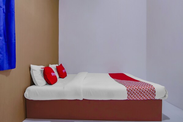 A bed with white and red bedding, a brown headboard, and a red pillow with white text.