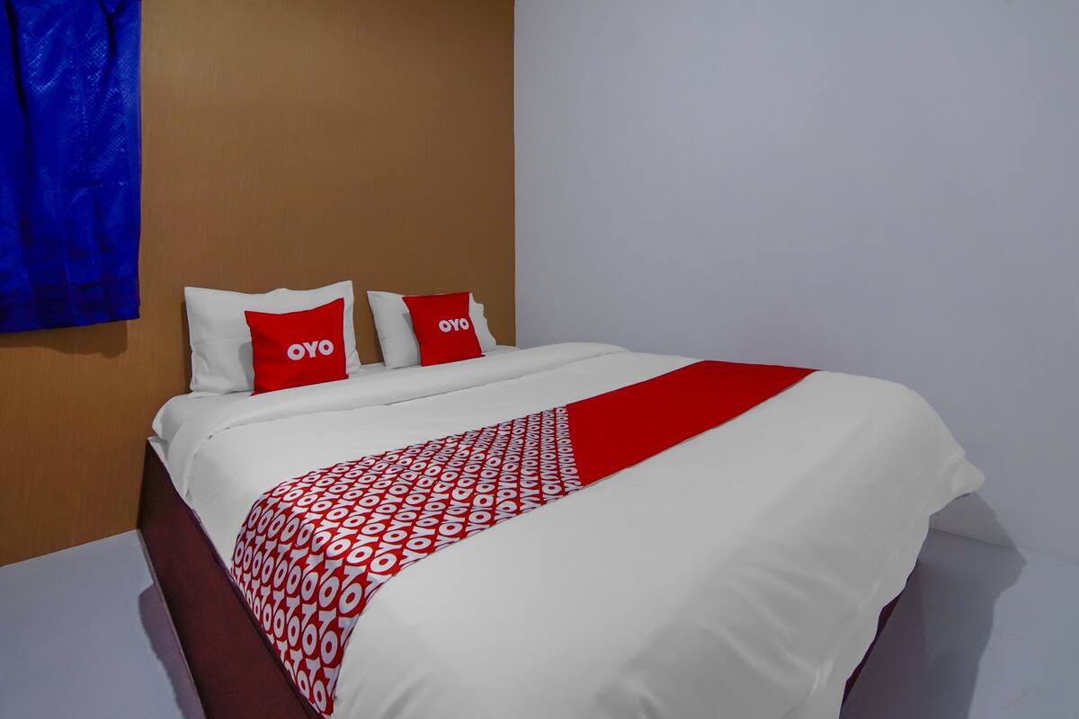 Ein Hotelzimmer mit einem Bett, zwei Kissen mit dem Logo "OYO" und einer roten und weißen Bettdecke.