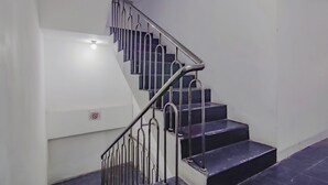 Eine Treppe mit Metallgeländern und dunklen Stufen, die zu einem Podest mit einer weißen Wand und einem roten Schild führt.