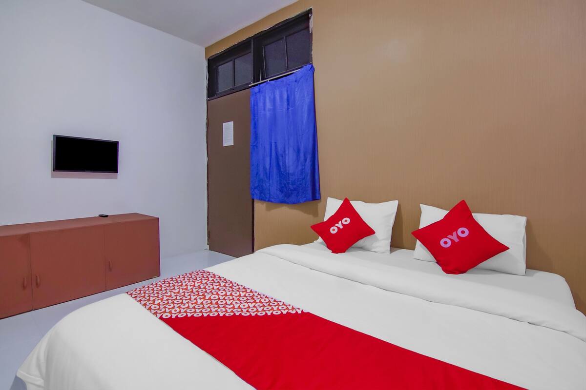 Ein Hotelzimmer mit Bett, Fernseher, Kleiderschrank und einem Fenster mit blauer Vorhang.