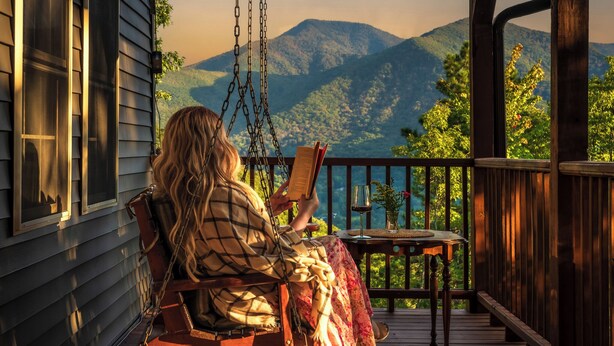 Una persona leyendo en un porche con vista a las montañas.