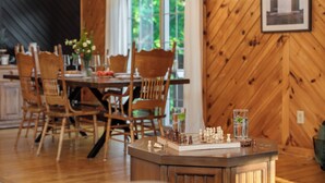 Un comedor de madera con un tablero de ajedrez, sillas y una mesa con un florero.