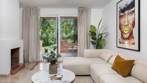A modern living room with a beige sofa, a round coffee table with a vase and book, a fireplace, and a large window with curtains. - Villa Federer: Best holiday rental in Marbella Old town (Marbella)