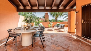A covered patio with a round table and chairs, a vase of flowers, and a view of palm trees and a building in the background. - Villa Federer: Best holiday rental in Marbella Old town (Marbella)