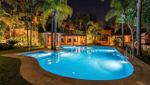 A swimming pool surrounded by palm trees and a building with a thatched roof. - Villa Federer: Best holiday rental in Marbella Old town (Marbella)