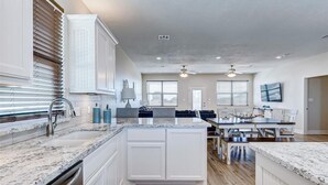 A spacious kitchen with white cabinetry, granite countertops, and a central island. There are two ceiling fans and a dining area with a table and chairs. - Laguna Cove Cabin, Canal Front (Bolivar)