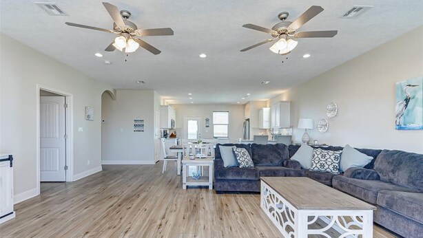 A spacious living room with a dark grey sectional sofa, a white coffee table, and two ceiling fans. - Laguna Cove Cabin, Canal Front (Bolivar)