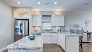 A modern kitchen with white cabinetry, a stainless steel refrigerator, a granite countertop, and a wooden floor. - Laguna Cove Cabin, Canal Front (Bolivar)