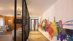 Ein Hotelgang mit moderner Ausstattung, darunter ein farbenfrohes abstraktes Wandbild und zeitgemäße Möbel.