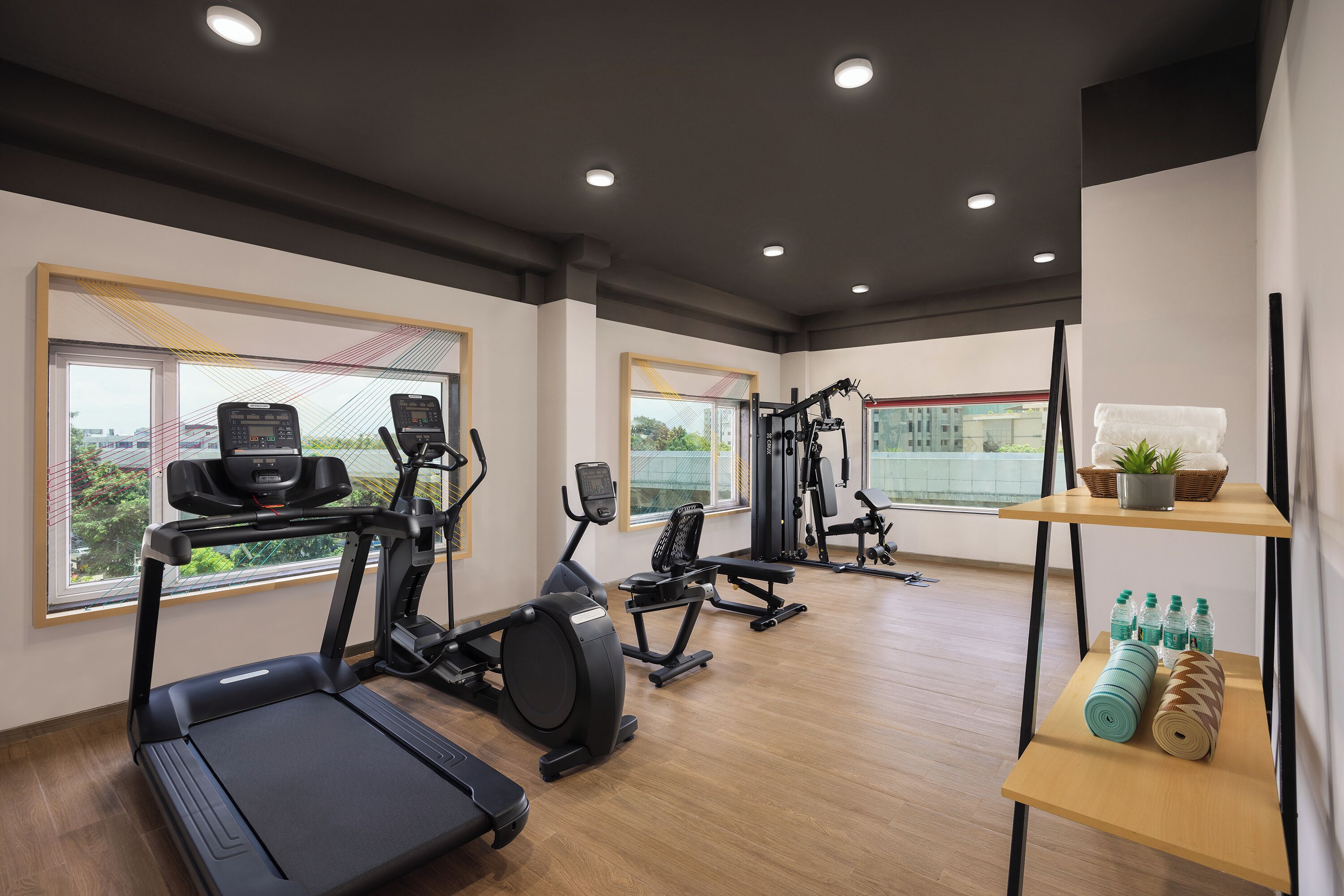 Une salle de sport moderne équipée de tapis de course, de vélos elliptiques et de poids libres. De grandes fenêtres laissent entrer la lumière naturelle et offrent une vue sur la ville.