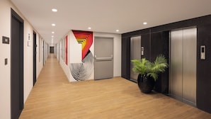 Ein moderner Hotelkorridor mit Holzboden, einem großen abstrakten Wandbild und zwei Aufzügen.
