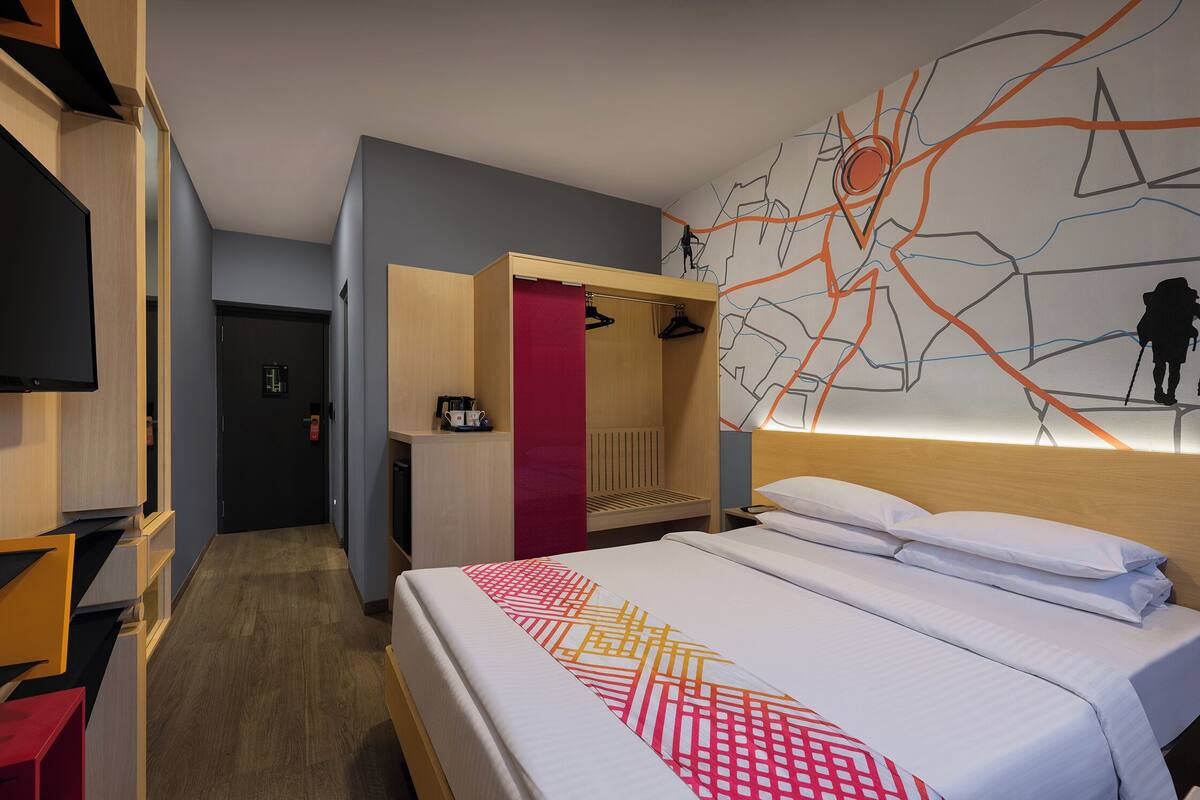 A hotel room with a bed, a TV, a wardrobe, and a wall with a map design.