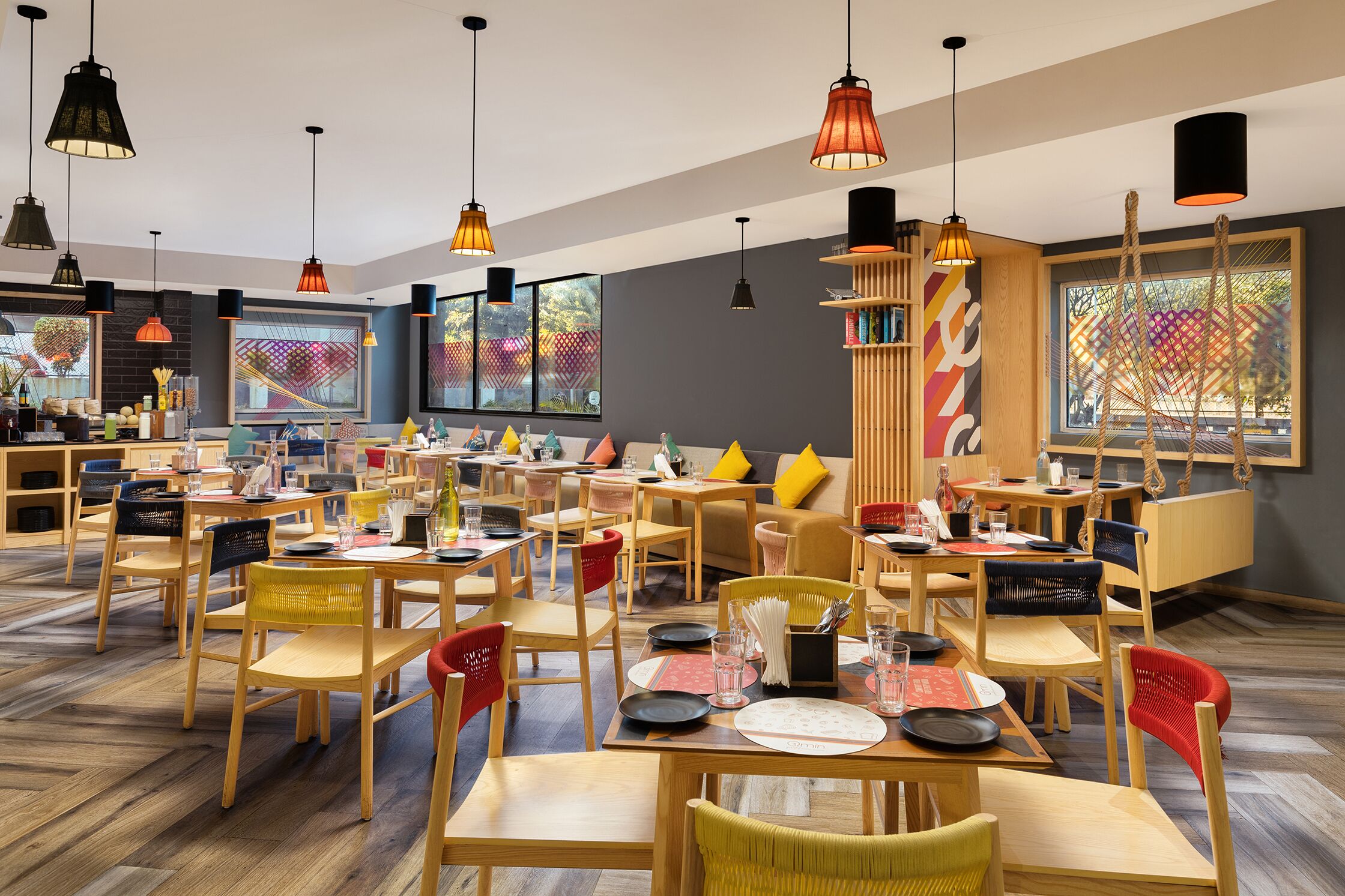 A modern restaurant with wooden furniture, multiple dining tables, and hanging pendant lights.