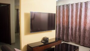 Una sala de estar con una televisión de pantalla plana montada en la pared, una mesa de centro de madera oscura y una cortina estampada.