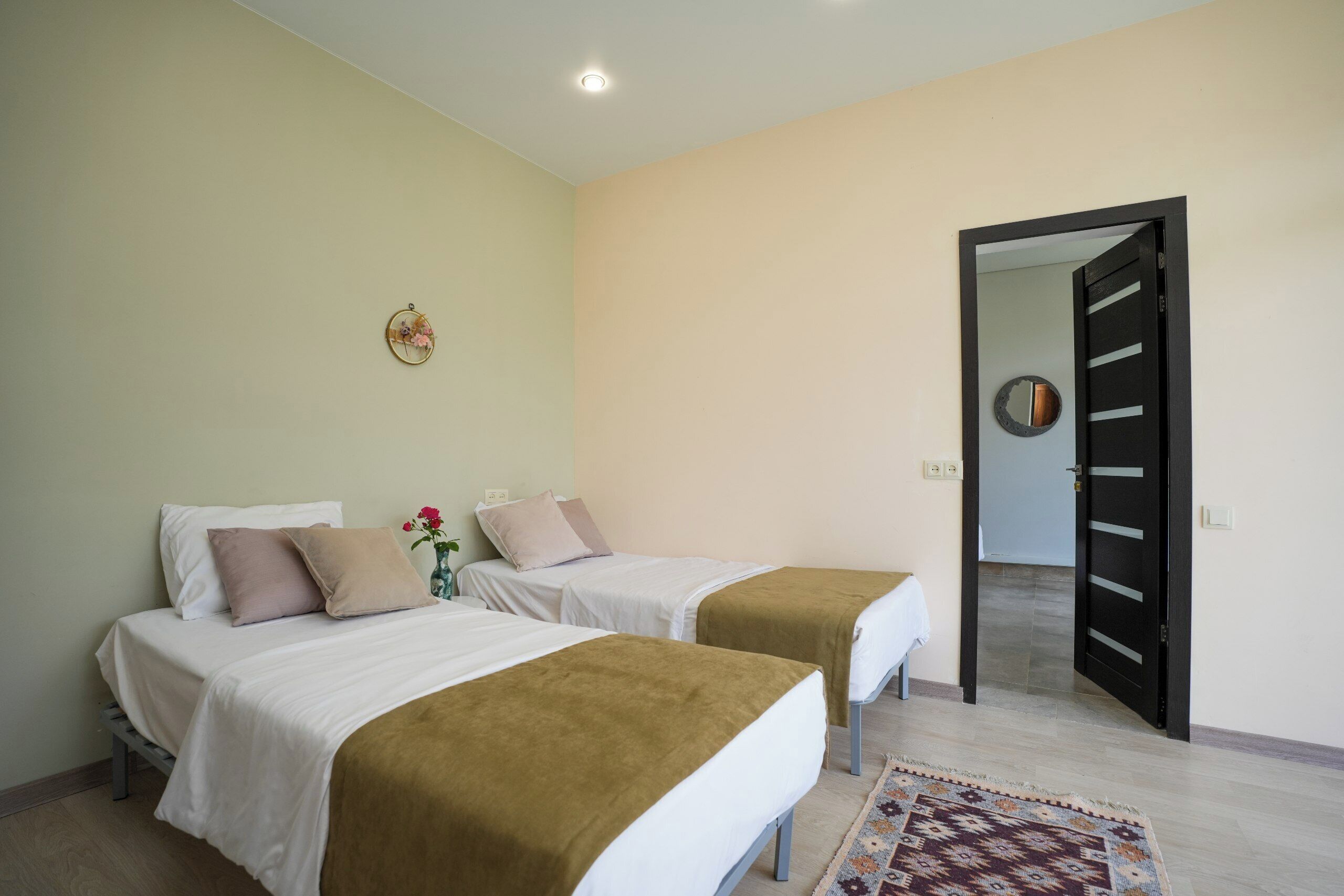 A room with two beds, a small table with a vase, and a door leading to another room.