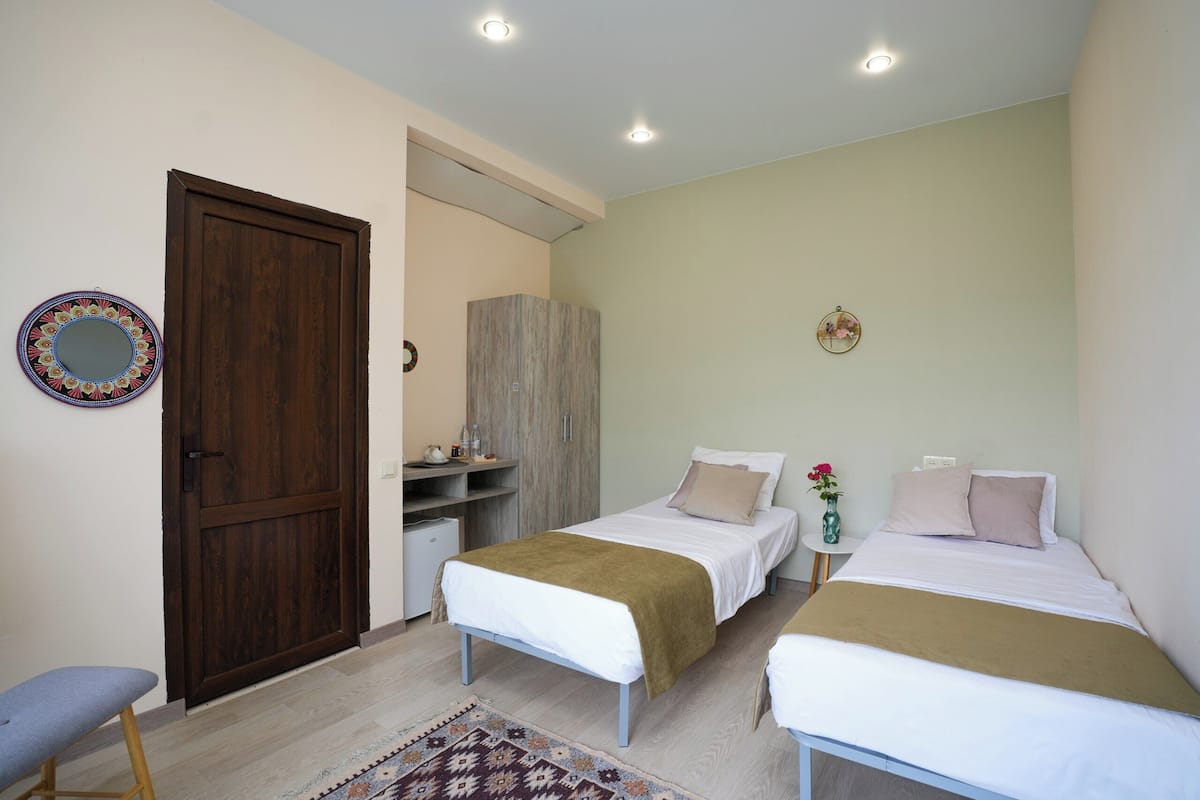 A bedroom with two beds, a wooden wardrobe, a small desk, and a mirror on the wall.