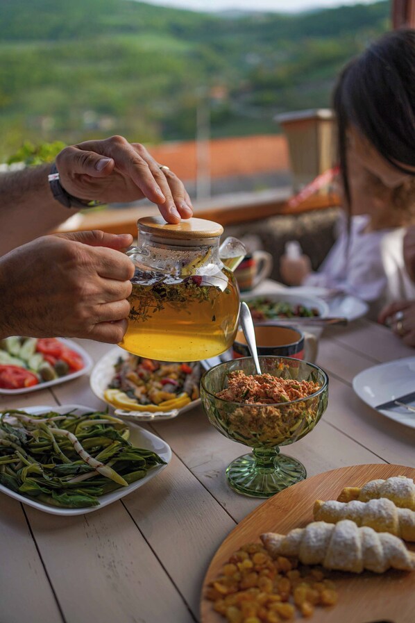 A person pouring a drink from a jar into a glass. There are plates of food, including a salad and a dish with nuts, on the table. - Chamich Guesthouse (Debet)