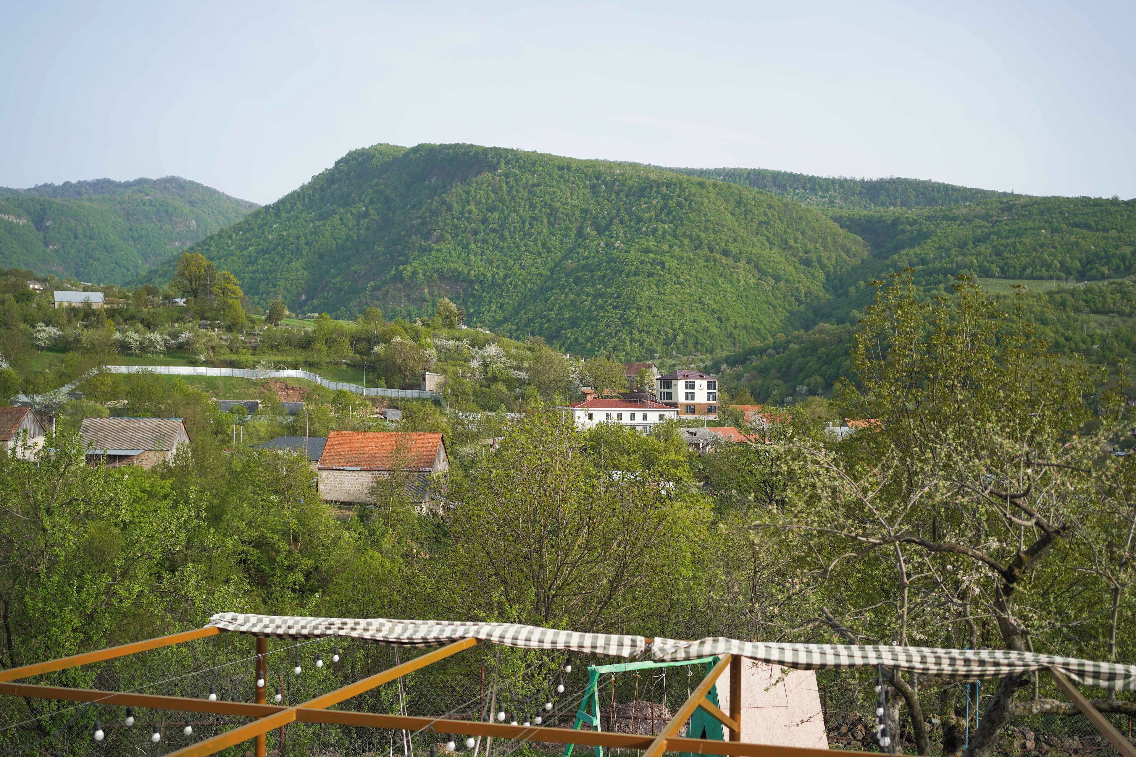 A rural landscape with houses, a checkered awning, and a green metal structure.