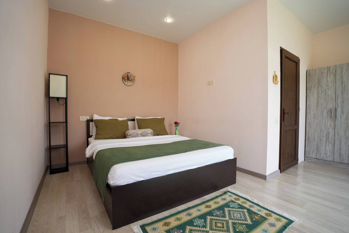 A bedroom with a bed, a bedside table, a lamp, and a door.