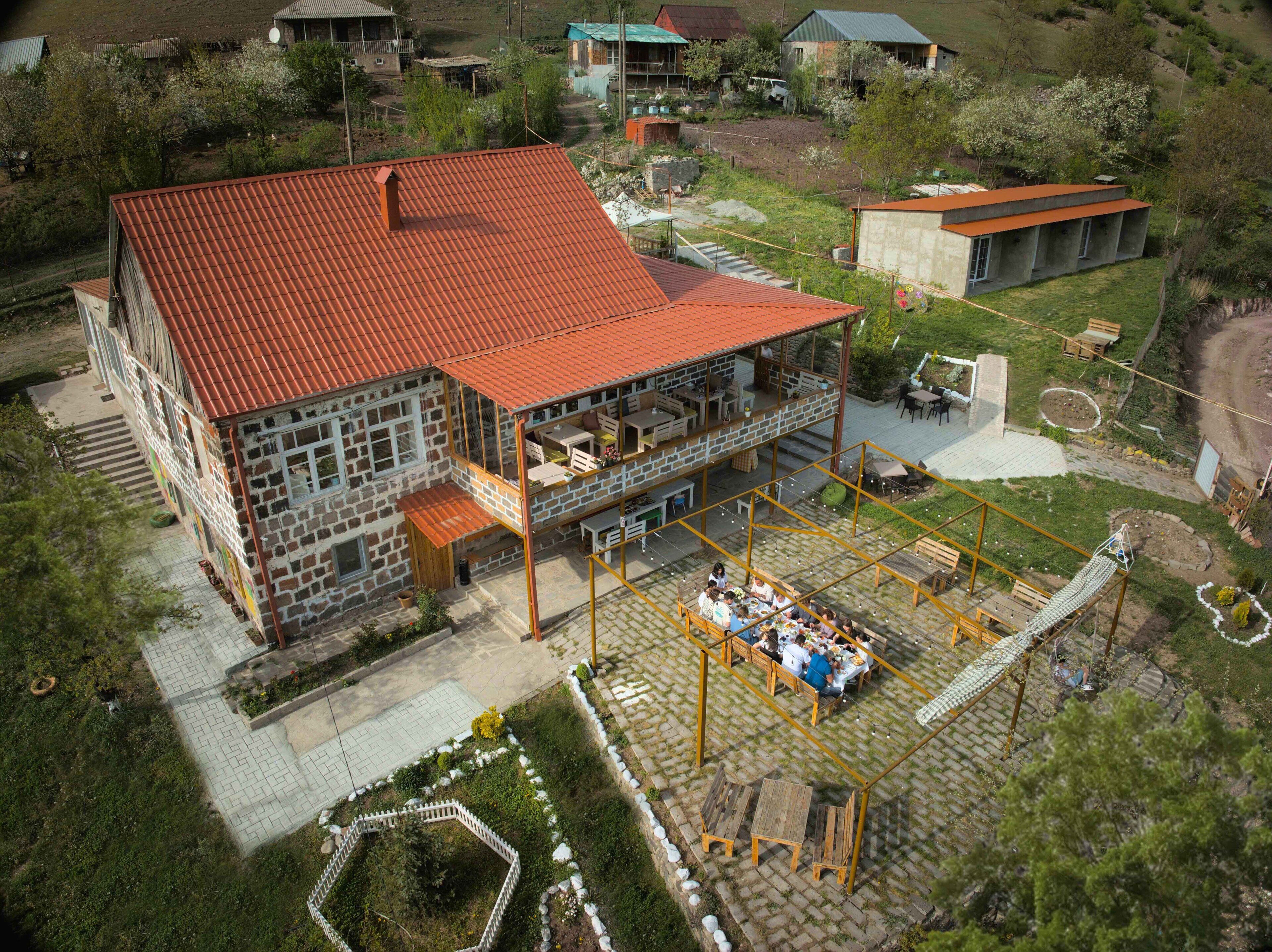 A large stone building with a red roof, a covered outdoor dining area, and a swimming pool.