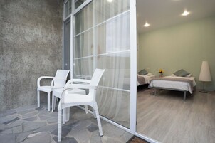 Una habitación con suelo de piedra, dos sillas blancas, una cama con almohadas y una lámpara.
