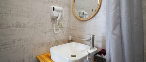 A bathroom with a white sink, a wooden countertop, a round mirror, and a hairdryer on the wall.