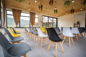 Un salón de conferencias con filas de sillas modernas, ventanas amplias con cortinas y plantas colgantes.