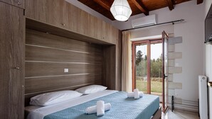 Una camera da letto con una testiera in legno, un letto con copripiumino blu, cuscini bianchi e due asciugamani arrotolati. C'è una porta scorrevole in vetro che dà su un balcone.