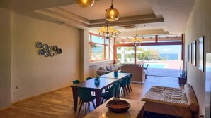 Een ruime woonkamer met een eettafel, stoelen, een bank en uitzicht op de omgeving.